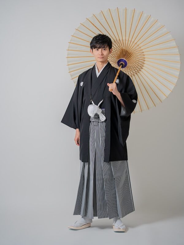 白い番傘を手に持ち、洗練された和の装いを見せる新郎のポートレート
