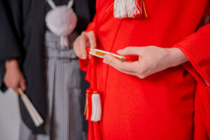 赤い着物を着た女性が手に持つ小物と、後ろにいる男性の姿。