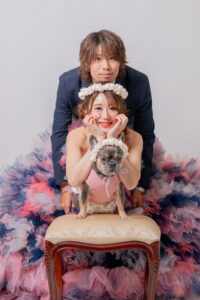 カラフルなフリルのドレスを着た女性とスーツを着た男性が椅子の上に座り、犬を抱いている写真。