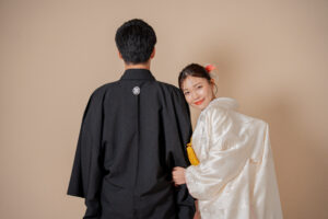 黒い和装を着た男性と白い和装を着た女性が背中を向け合っているシーン。女性は微笑んでいる。