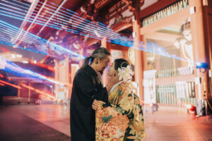 伝統的な和装を着たカップルが近づいている様子。背景には色とりどりの光が映し出されている。