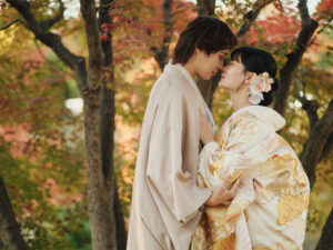 和装を着た二人が紅葉の中で寄り添い、顔を近づけているシーン。