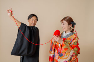黒い衣装を着た男性が赤い糸を持ち、色鮮やかな着物を着た女性がそれを見つめているシーン