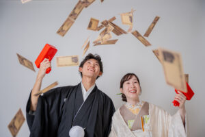 男性と女性が和装を着て、手に持った赤い道具から紙を投げている様子。