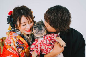 和装を着たカップルが、着物を着たフレンチブルドッグを抱きしめている。