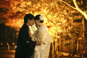 秋の紅葉の中で和装を着た二人が寄り添う様子。柔らかな光に包まれたロマンティックなシーン。