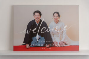 和装を着た男女が座り、ウェルカムボードの前で微笑んでいる。背景はシンプルで、文字がデザインされている。