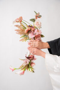 手に持たれた色とりどりの花束。ピンクの花や緑の葉が組み合わさった美しいアレンジメント。