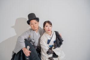 和装を着た男女がカメラに向かってポーズをとっている。男性は帽子をかぶり、女性は伝統的な白い着物を着用している。