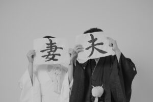 和装を着た男女がそれぞれ「妻」と「夫」と書かれた紙を持っている。