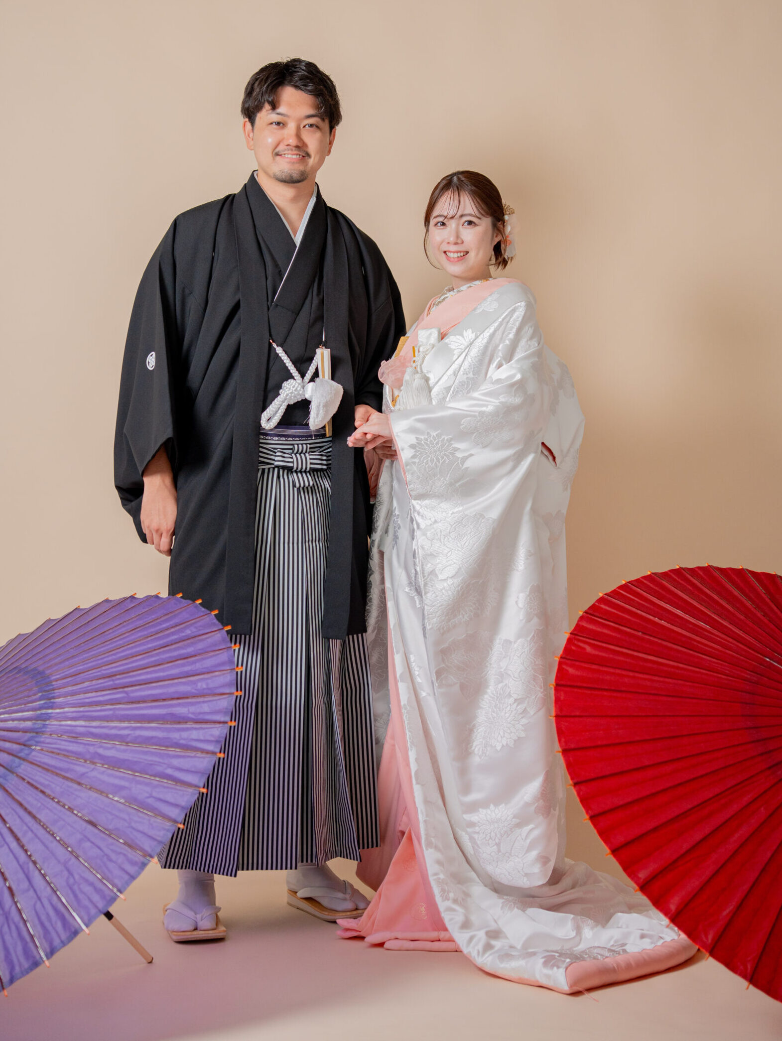 紅白の番傘を背景に、黒紋付袴の新郎と並んで微笑む和装カップルショット