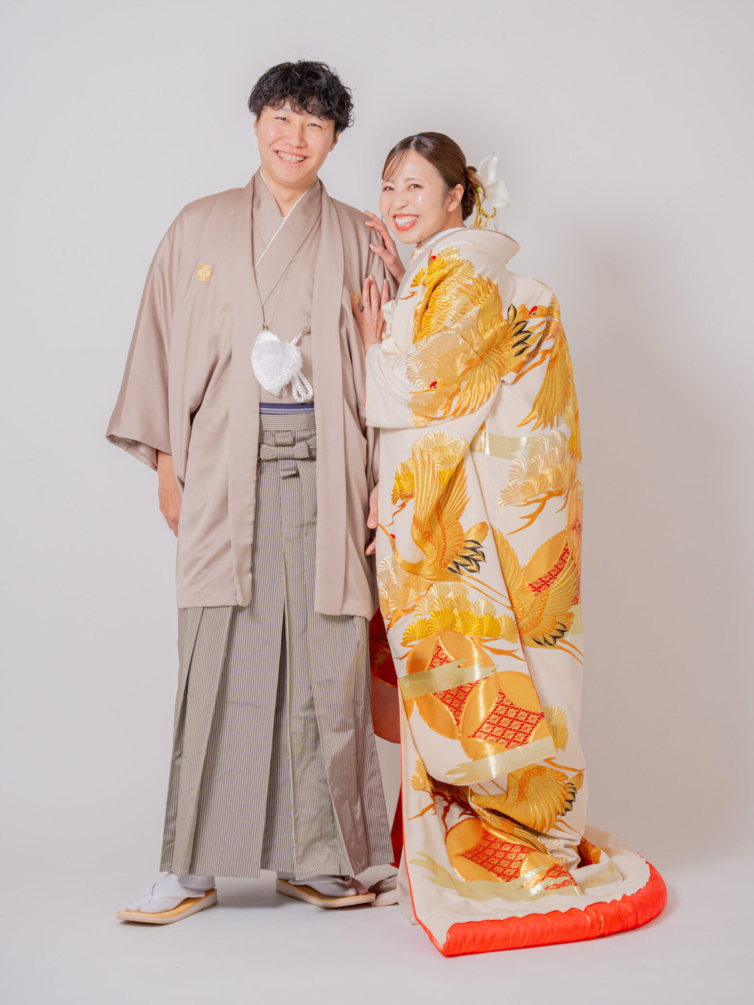 上品なカフェラテカラーの紋付姿の新郎にゴールドの色打掛の花嫁様が寄りかかるショット 和装カップルの王道立ち姿