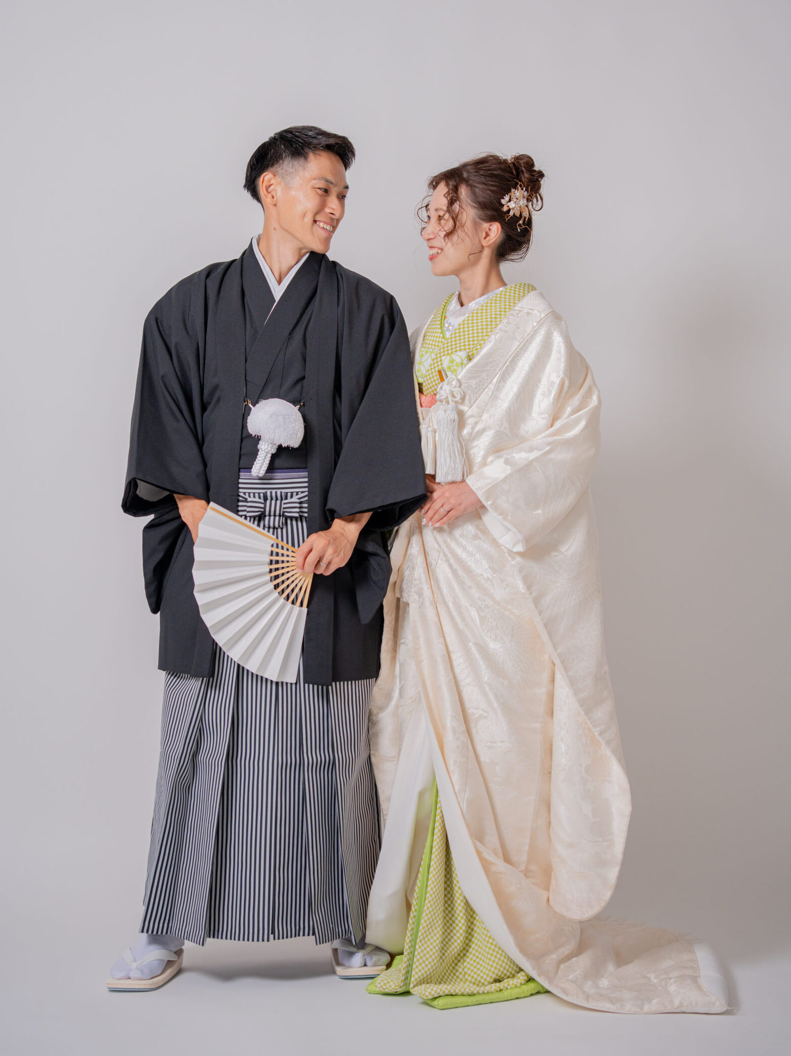若草色の掛下を合わせた花嫁と黒紋付袴の新郎が見つめ合う、和やかなカップルショット