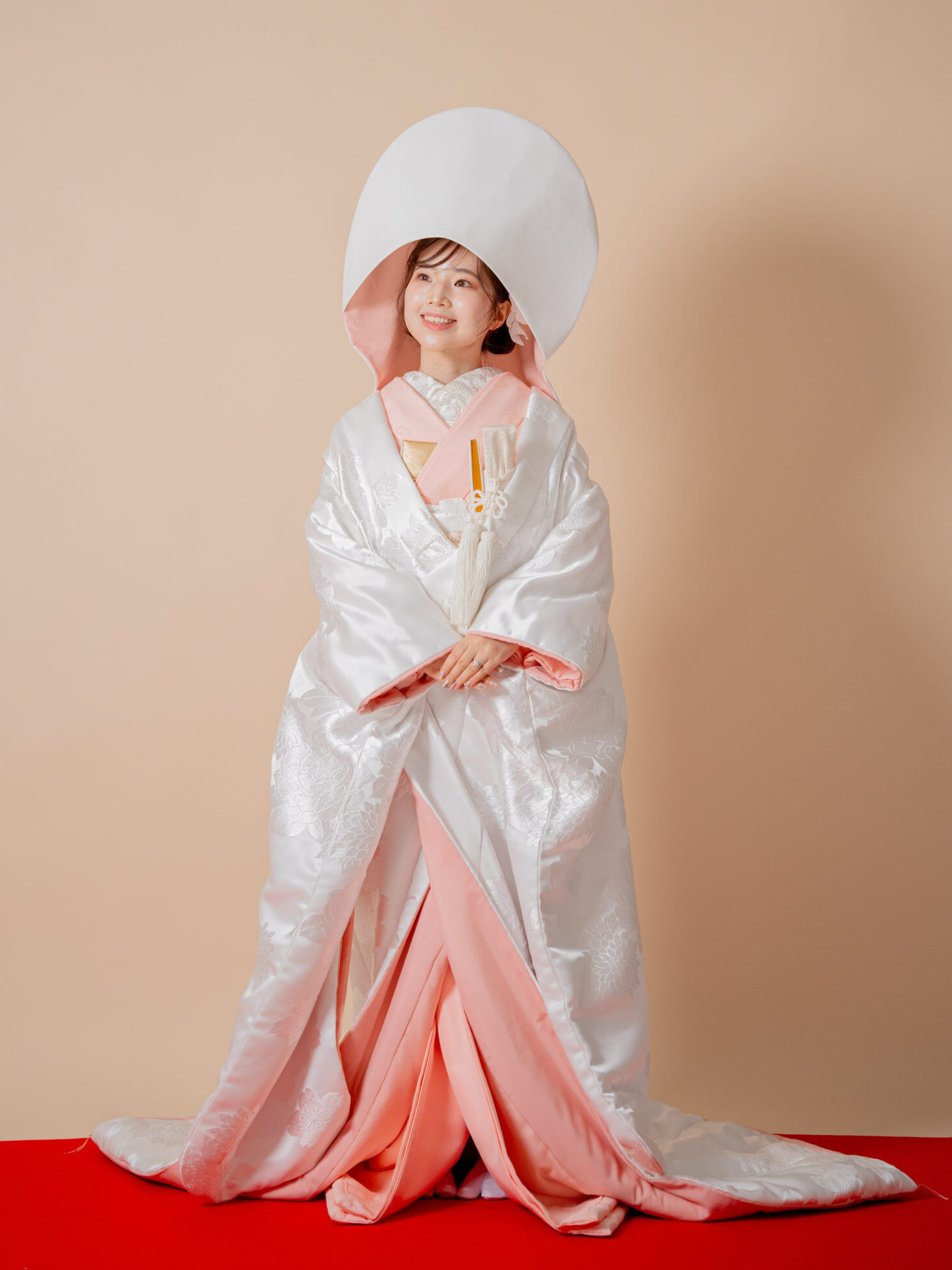 ピンクの掛下と綿帽子を合わせ、赤い絨毯に佇む可憐な花嫁の全身姿