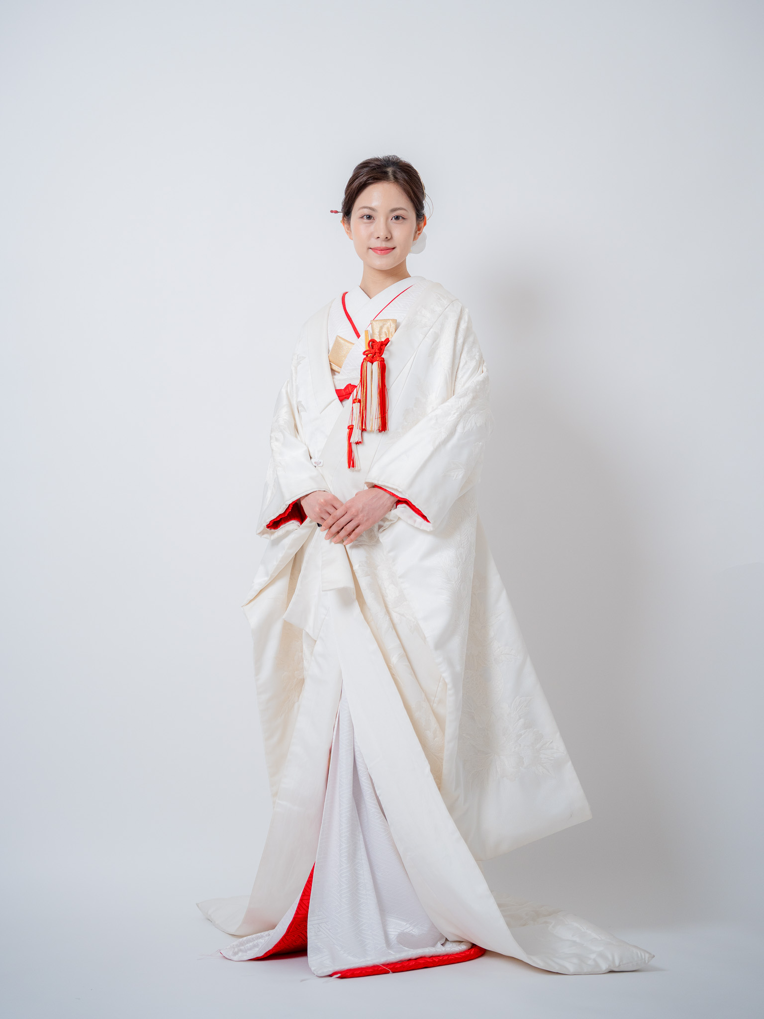 赤比翼の白掛下と純白の白無垢を合わせ、手を重ねて微笑む花嫁の正面立ち姿