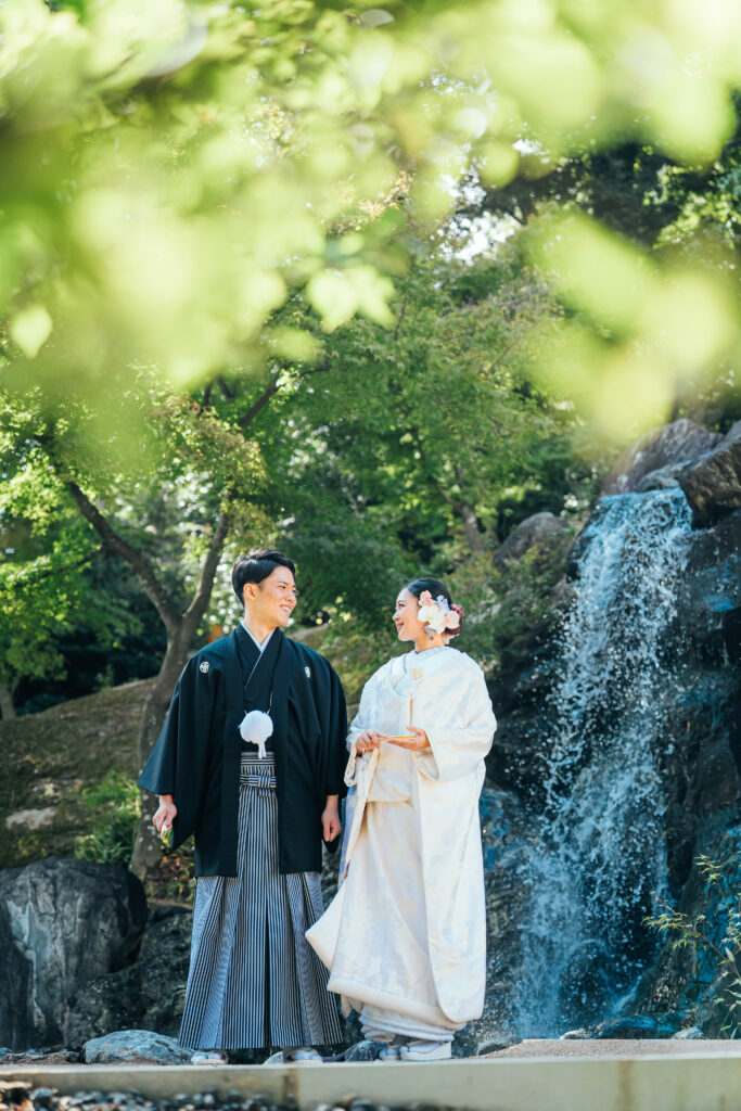 滝が流れる背景での和装前撮りロケーションの様子。白無垢の花嫁と見つめ合う新郎