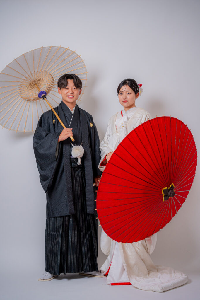 紅白の番傘を持ってポージングする白無垢姿の花嫁と新郎