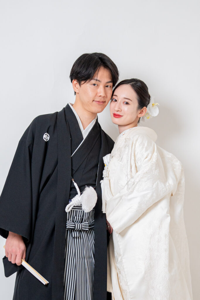 頬と頬を寄せ合う白無垢姿の花嫁と手に末広を持って立つ新郎のポーズ