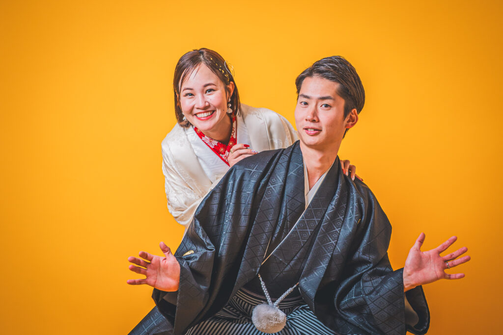 オレンジ背景。新郎の後ろから笑顔の新譜がのぞき込み。白打掛。②ショット