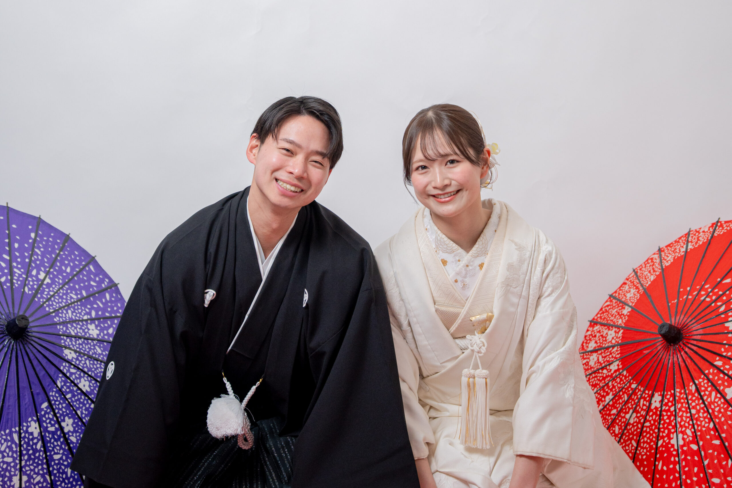 紋付き袴、白無垢で正座の2ショット。青色と赤色の番傘、笑顔