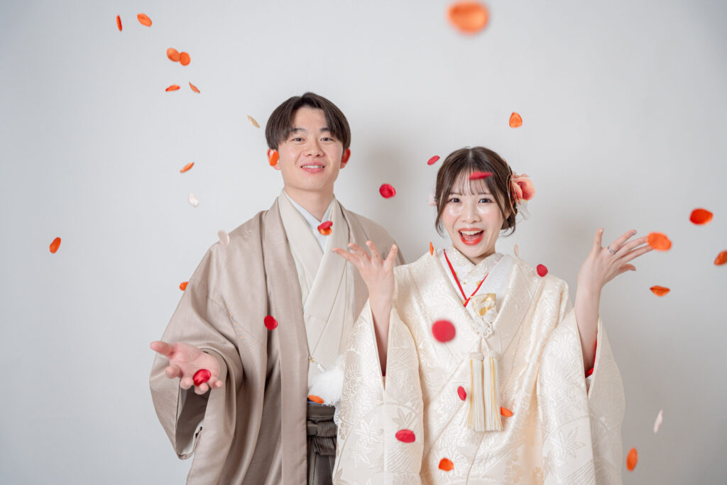 和装の2人でコンフェッティ。白系統の衣装・背景に、赤色のコンフェッティと新婦の口紅が映えるショット