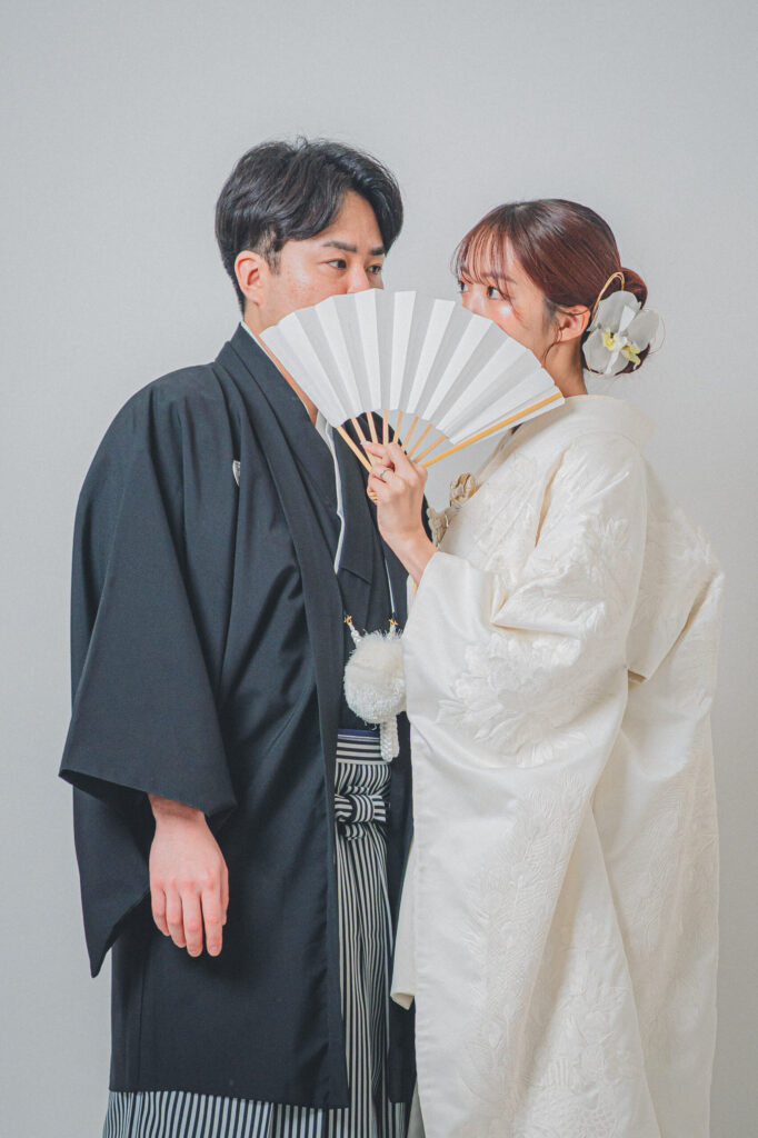 和装の2人が扇子で口元を隠したおしゃれな2ショット。紋付き袴、白無垢