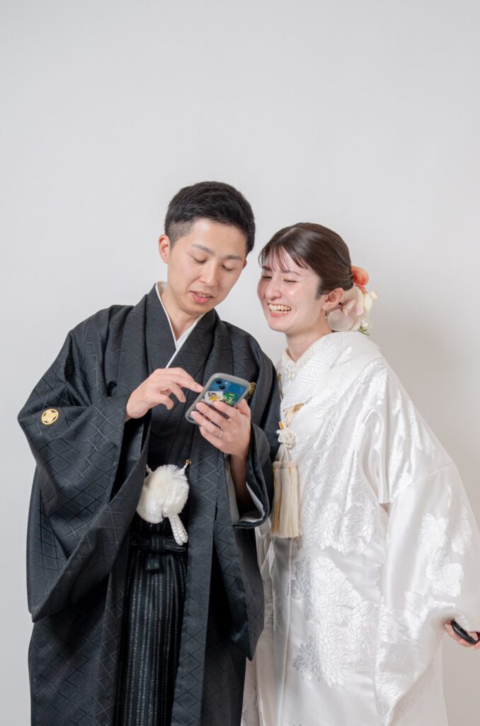 笑顔で携帯電話をのぞき込む和装の二人。紋付き袴、白無垢