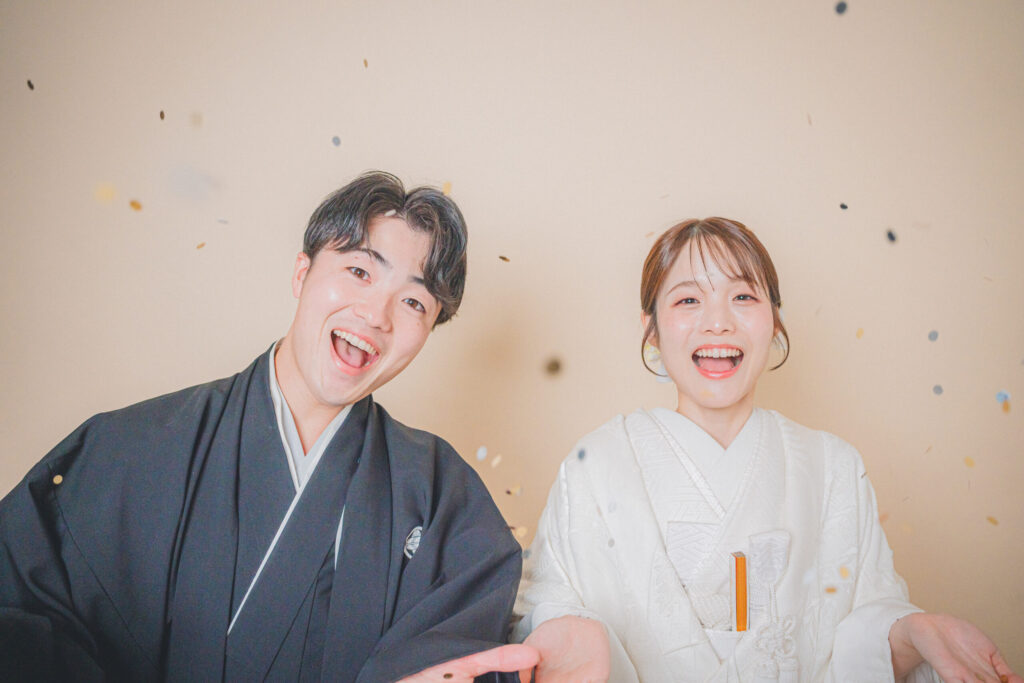 和装の新郎新婦がコンフェッティで笑顔の2ショット。紋付き袴、白無垢