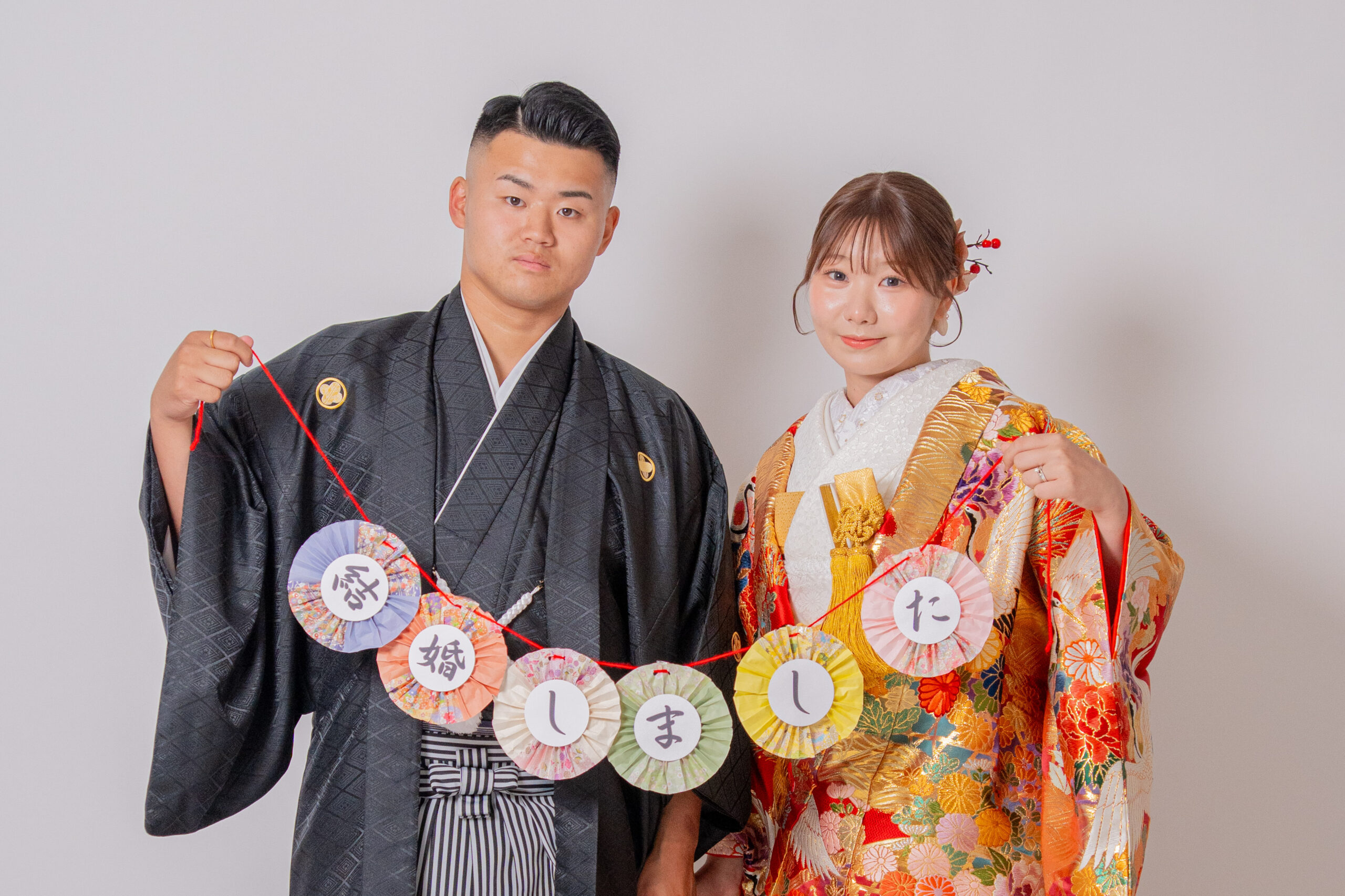 和装の新郎新婦が「結婚しました」ガーランドをもって笑顔のショット。少し緊張気味。紋付き袴、色打掛