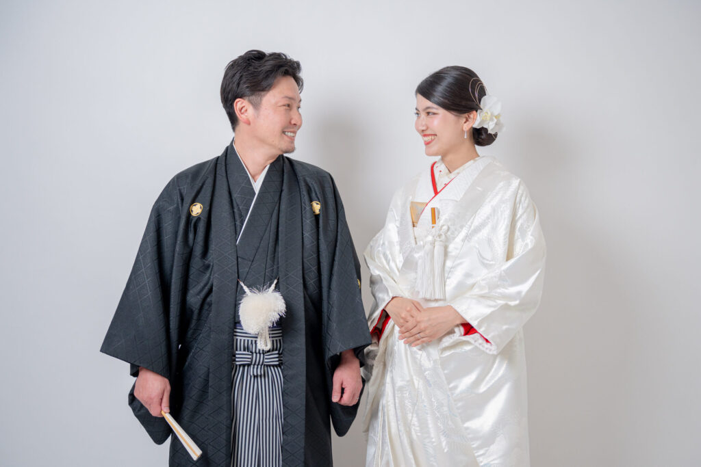 和装の新郎新婦が見つめい笑顔のショット。
黒髪に赤リップが映える。紋付き袴、白無垢