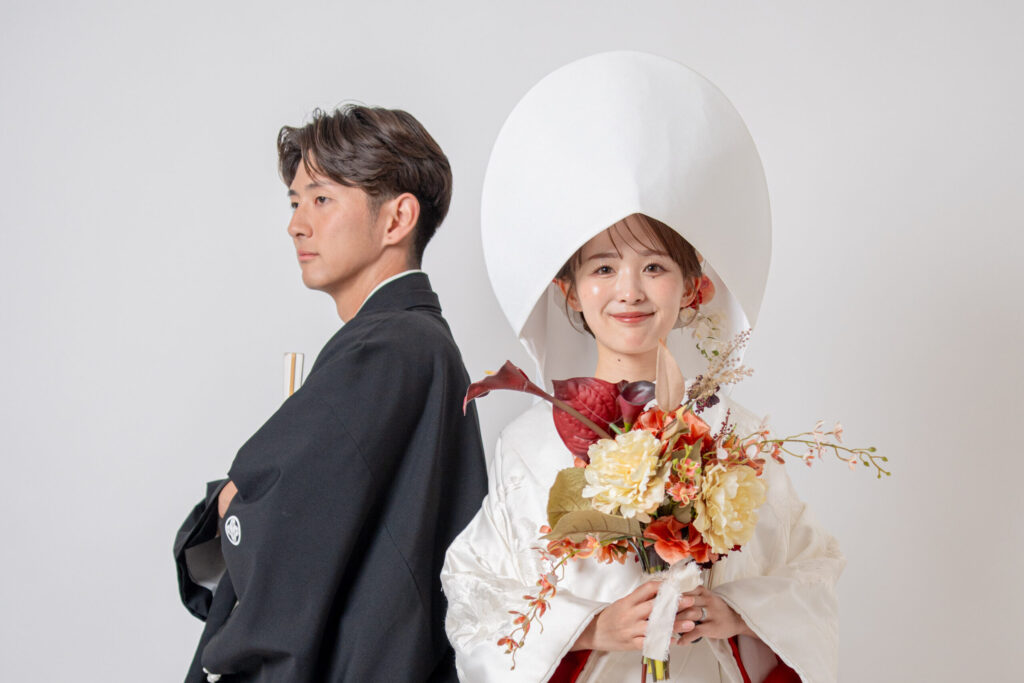 和装の新郎新婦。綿帽子の新譜が色鮮やかなブーケを持って笑顔。新郎は目線外し。粋なショット