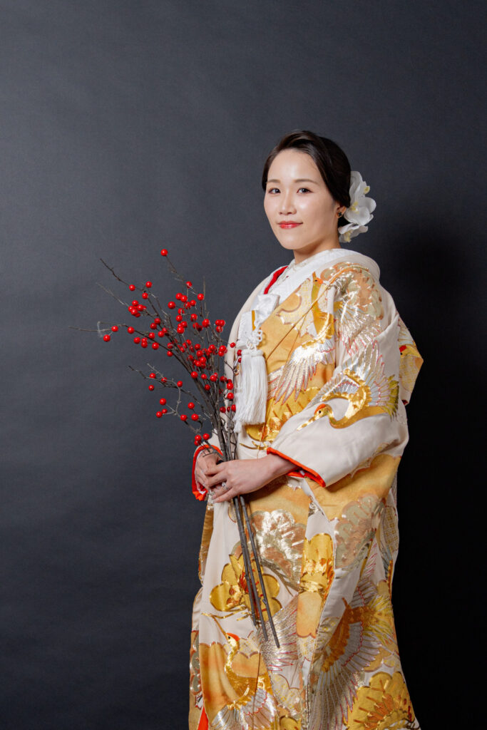 ゴールドの豪華な色打掛の新婦ソロショット。白い旗に、赤い実のブーケのコントラストが美しい