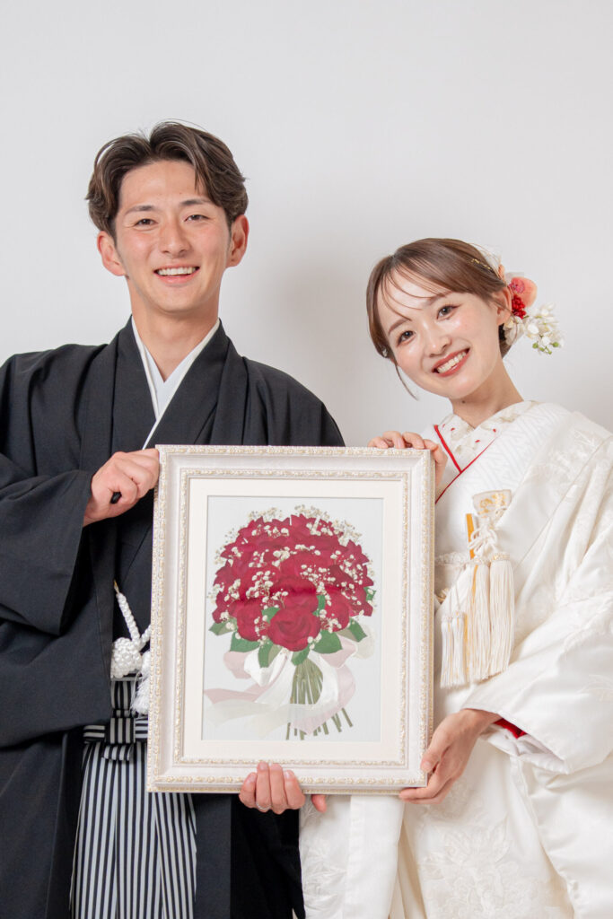 和装の新郎新婦が、赤いバラの絵を持って結婚報告。紋付き袴、白無垢