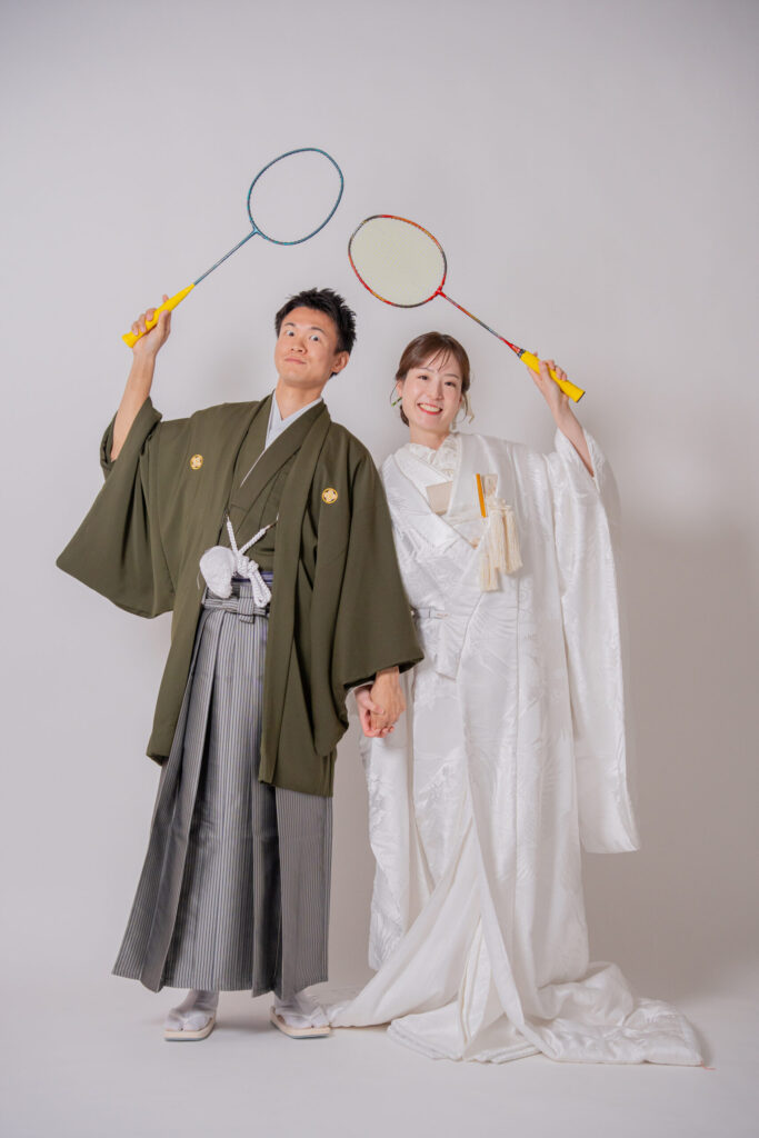 和装の新郎新婦が趣味のバトミントンのラケットを持ったおそろいショット。