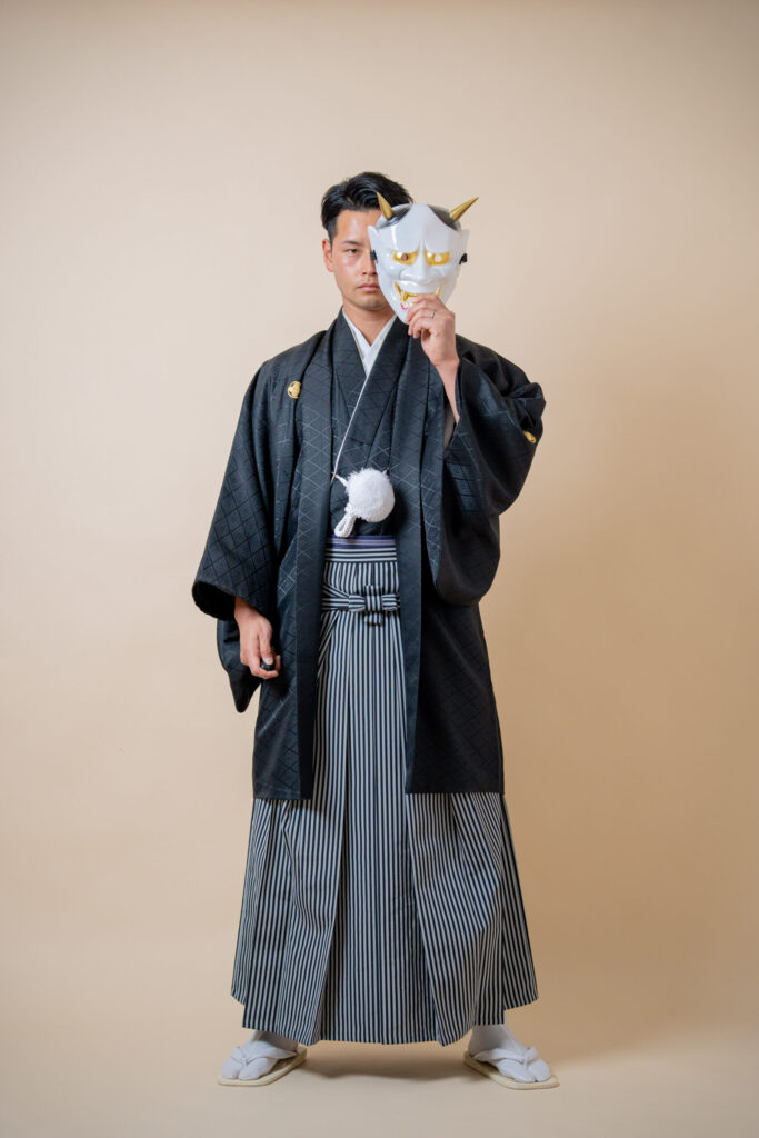 和装の新郎がお面で顔を半分隠した真顔ショット。紋付き袴