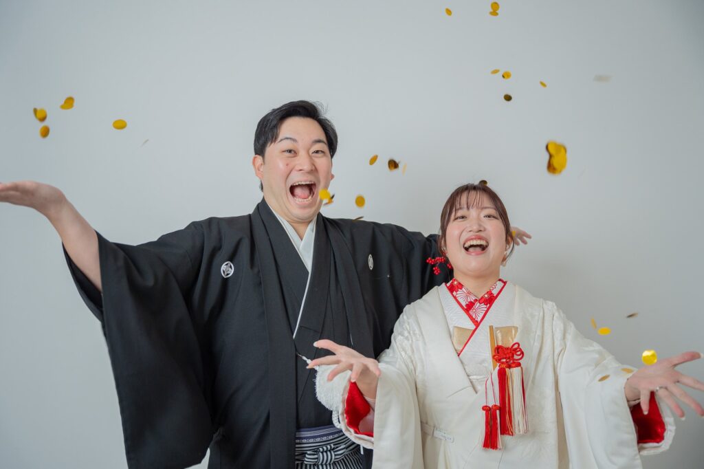 金色のコンフェッティが舞う中で大笑いする白無垢の花嫁と紋付袴の新郎
