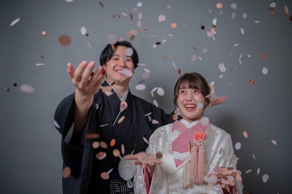 白無垢の花嫁と紋付袴の新郎がコンフェッティを投げて笑い合う瞬間
