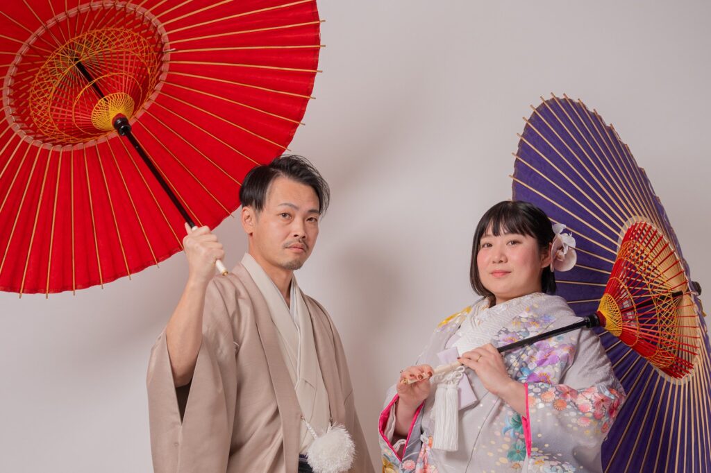 赤と紫の和傘を持つ色打掛の花嫁と羽織袴の新郎の和装前撮り