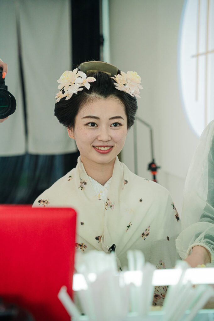 鏡の前で日本髪のヘアメイクを仕上げて笑顔を見せる花嫁