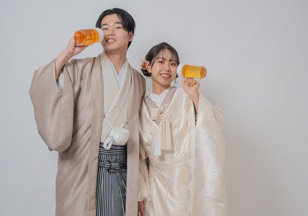 和装の新郎新婦がビールジョッキの小物を持っておどけたポーズをとる写真